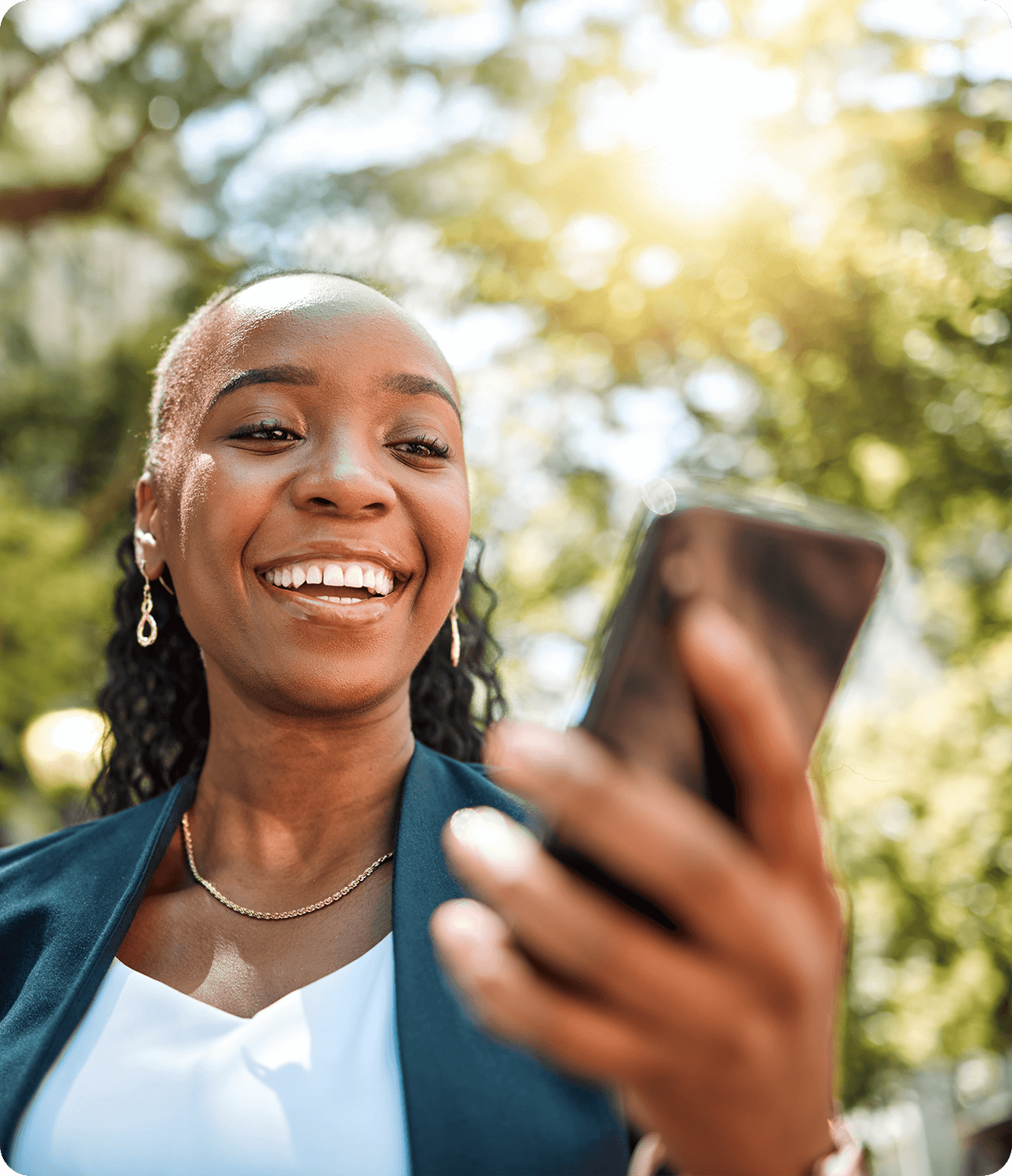 A woman smiling at her phone outside in the sunshine